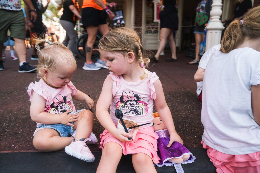 Toddler and Preschool girls sitting together eating ice cream on Main Street Magic Kingdom, Orlando, FL